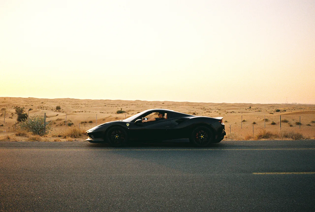 A black Ferrari driving past the dunes outside Dubai at golden hour